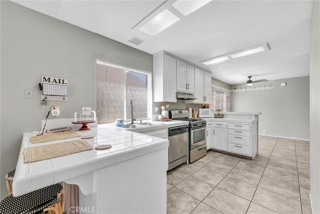 kitchen with visible vents, tile countertops, a peninsula, stainless steel appliances, and a sink