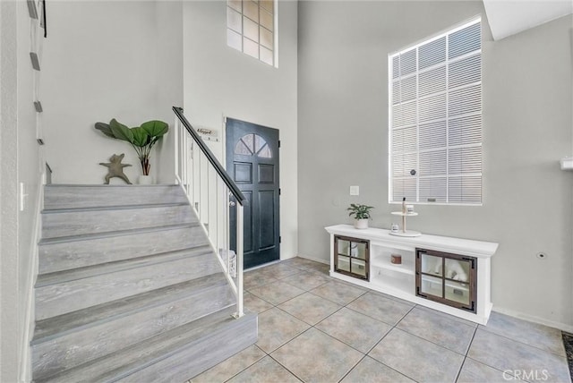 foyer entrance with light tile patterned floors, a towering ceiling, and stairs