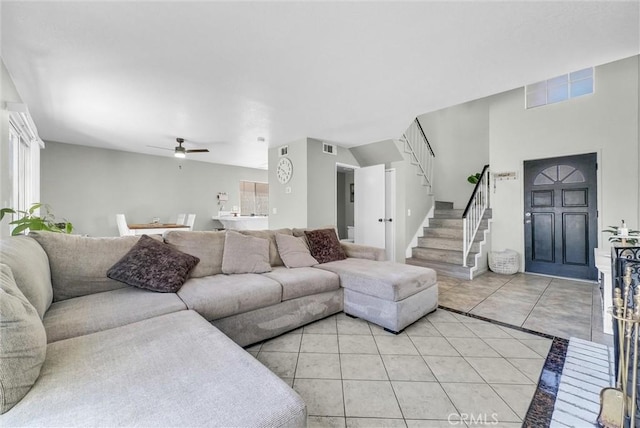 living area with light tile patterned floors, visible vents, a ceiling fan, a healthy amount of sunlight, and stairs