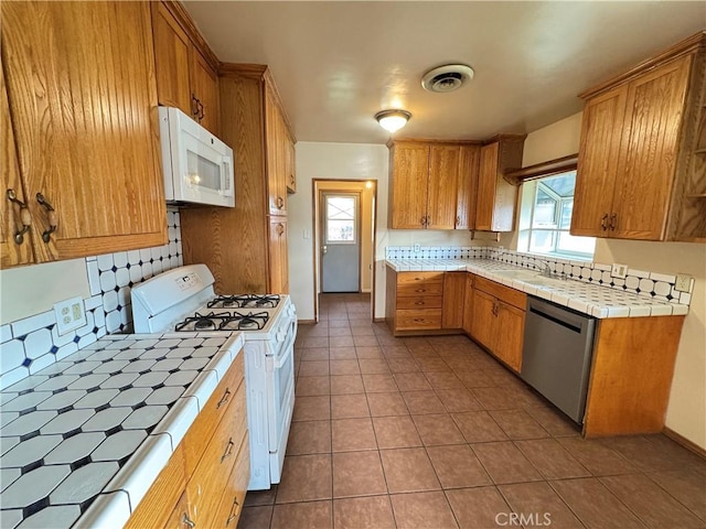 kitchen with tile counters, tasteful backsplash, visible vents, tile patterned flooring, and white appliances