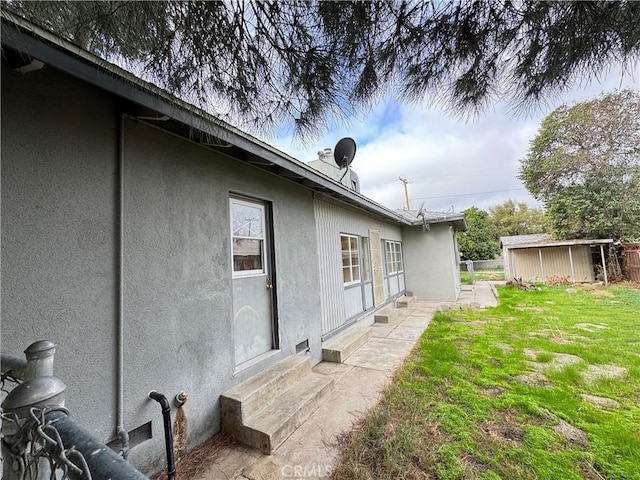 rear view of property featuring entry steps, a lawn, an outbuilding, and stucco siding