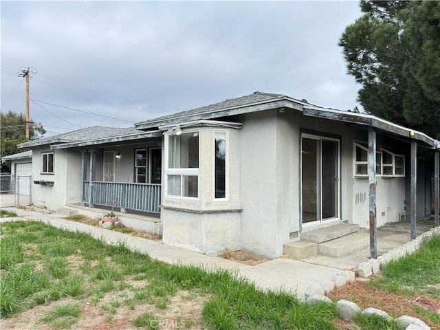 view of side of home featuring entry steps, covered porch, roof with shingles, and stucco siding