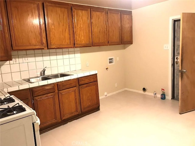 kitchen with brown cabinetry, white gas range oven, a sink, and tile counters