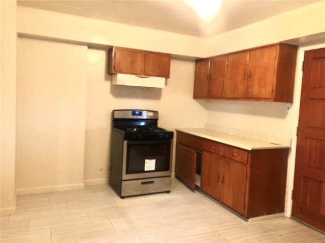 kitchen with light countertops, gas stove, brown cabinets, and under cabinet range hood