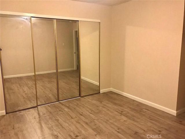 unfurnished bedroom featuring a closet, wood finished floors, and baseboards