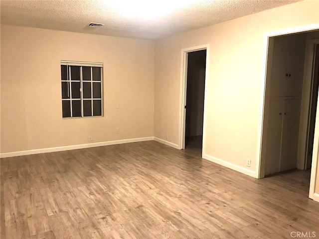 empty room with a textured ceiling, baseboards, and wood finished floors