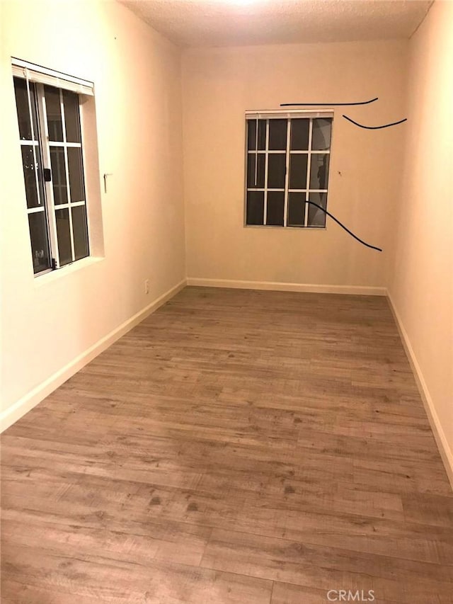 empty room featuring a textured ceiling, wood finished floors, and baseboards