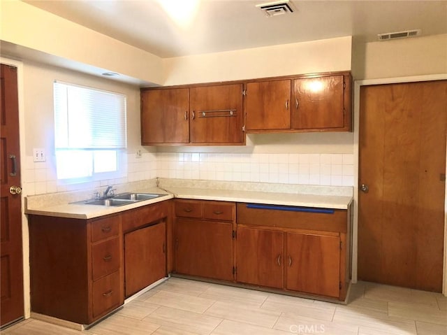 kitchen with a sink, visible vents, light countertops, brown cabinets, and tasteful backsplash