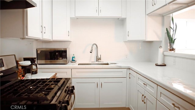 kitchen with stainless steel appliances, backsplash, white cabinets, a sink, and under cabinet range hood