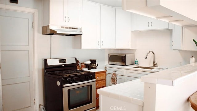 kitchen with tile countertops, appliances with stainless steel finishes, a sink, and under cabinet range hood