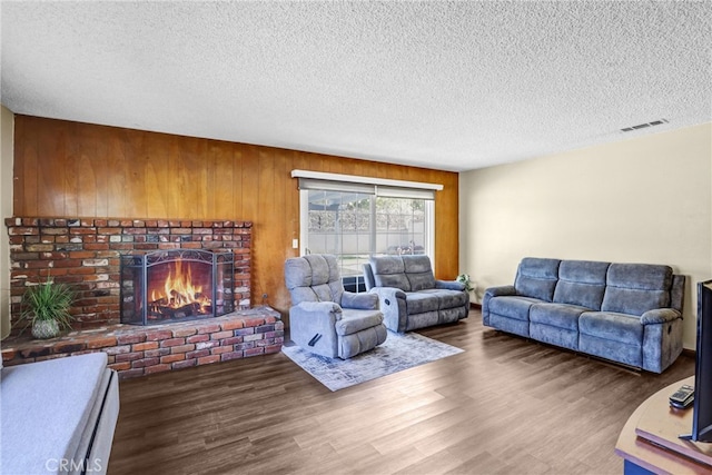 living room featuring a brick fireplace, a textured ceiling, visible vents, and wood finished floors