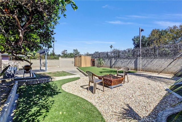 view of yard featuring an outbuilding, a patio area, a shed, a fenced backyard, and a fire pit