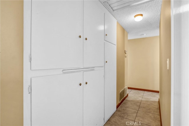 corridor featuring light tile patterned floors, baseboards, visible vents, and a textured ceiling