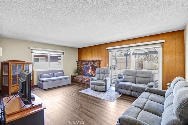 living room featuring a fireplace, wood walls, a textured ceiling, and wood finished floors