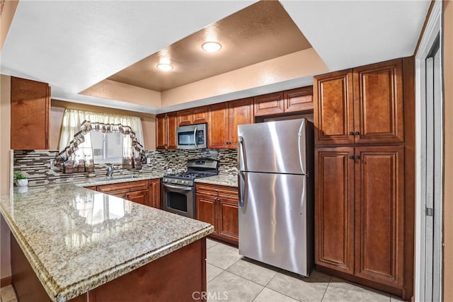 kitchen with a tray ceiling, backsplash, appliances with stainless steel finishes, a sink, and a peninsula