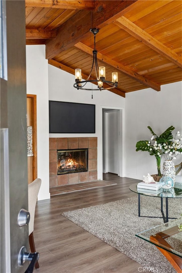 living area with vaulted ceiling with beams, a chandelier, wood finished floors, wood ceiling, and a tiled fireplace