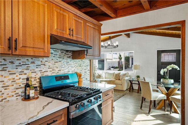 kitchen with decorative backsplash, vaulted ceiling with beams, stainless steel gas range, under cabinet range hood, and a notable chandelier