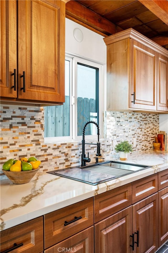 kitchen with light countertops, brown cabinetry, a sink, and beam ceiling