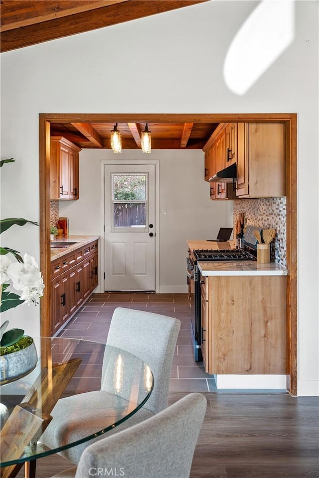 kitchen with beam ceiling, light countertops, backsplash, gas stove, and under cabinet range hood