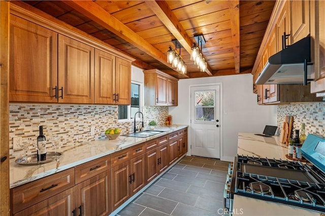 kitchen with under cabinet range hood, a sink, stainless steel range with gas cooktop, light stone countertops, and beamed ceiling