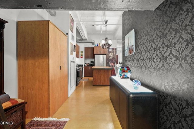 kitchen featuring wallpapered walls, appliances with stainless steel finishes, light countertops, concrete floors, and a notable chandelier