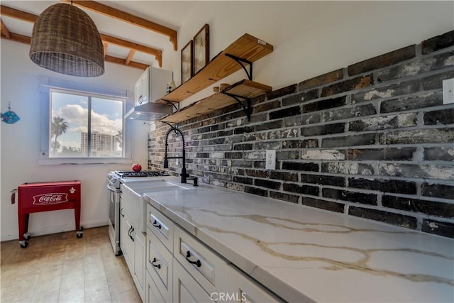 kitchen featuring light wood finished floors, white cabinets, brick wall, light stone countertops, and under cabinet range hood