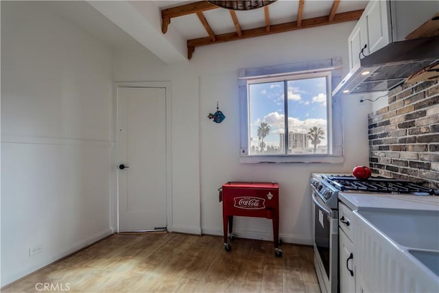 kitchen featuring stainless steel gas stove, beamed ceiling, light wood-type flooring, under cabinet range hood, and white cabinetry