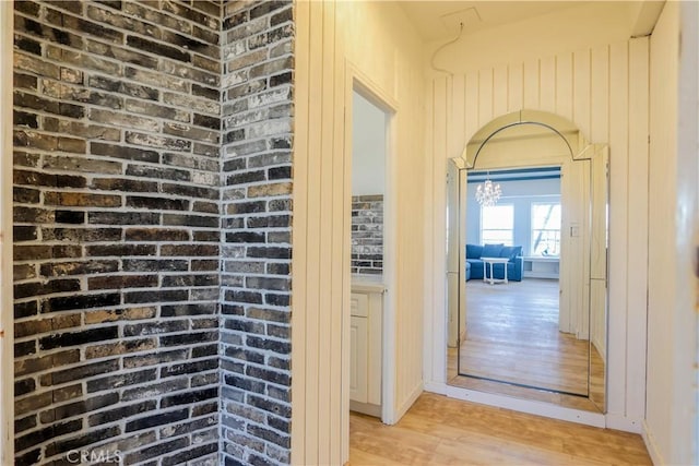 hallway featuring light wood-style floors, arched walkways, and brick wall