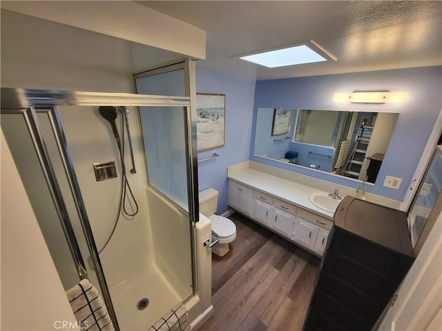 bathroom with toilet, a skylight, wood finished floors, vanity, and a shower stall