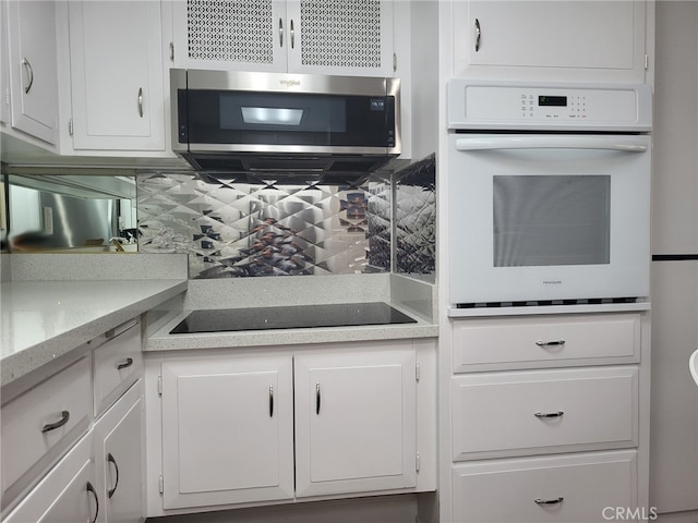 kitchen with white oven, white cabinets, stainless steel microwave, and decorative backsplash