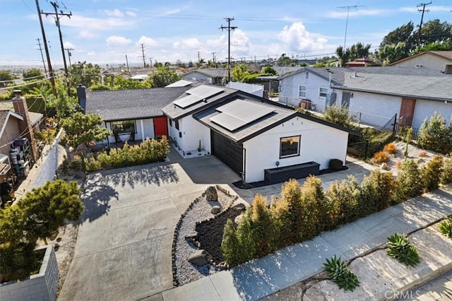 view of front facade featuring roof mounted solar panels, fence, concrete driveway, and a residential view