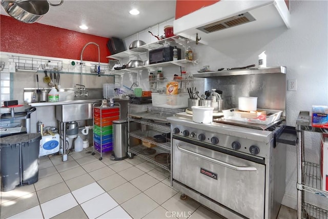 kitchen featuring tile patterned floors, a textured wall, and high end stainless steel range