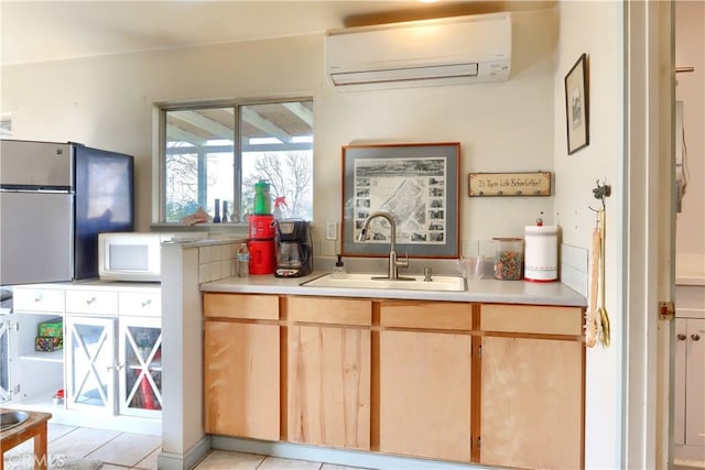 kitchen with light countertops, white microwave, freestanding refrigerator, a sink, and a wall mounted air conditioner