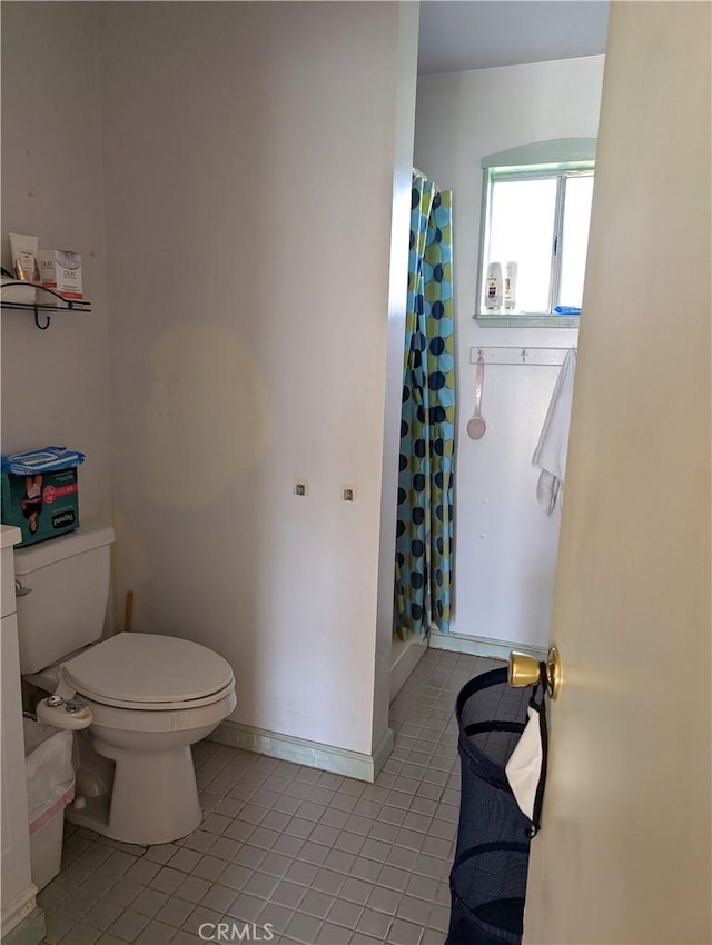 bathroom featuring baseboards, a shower with shower curtain, toilet, and tile patterned floors