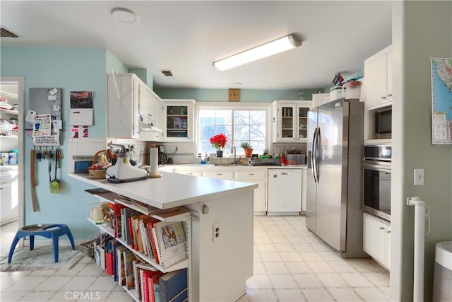 kitchen with appliances with stainless steel finishes, white cabinets, a sink, a peninsula, and under cabinet range hood