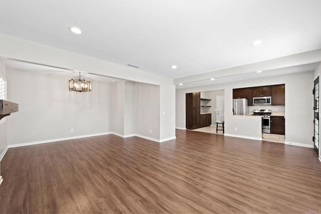 unfurnished living room with visible vents, baseboards, an inviting chandelier, and wood finished floors