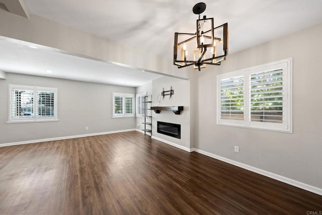 unfurnished living room with a chandelier, a glass covered fireplace, baseboards, and dark wood-style flooring