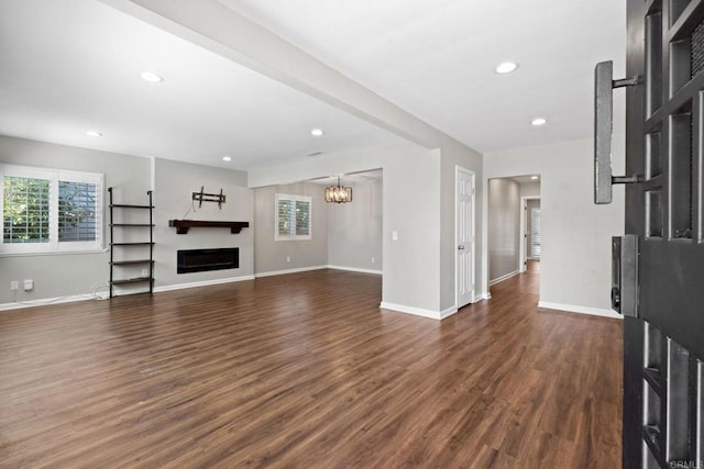 unfurnished living room featuring baseboards, recessed lighting, a fireplace, dark wood-style flooring, and a notable chandelier