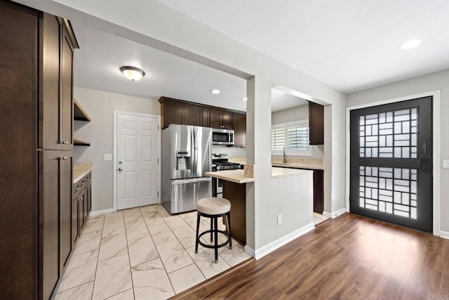 kitchen with a breakfast bar area, stainless steel appliances, dark brown cabinetry, marble finish floor, and a center island