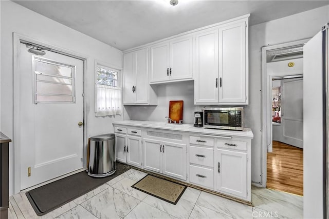 kitchen with stainless steel microwave, white cabinets, a sink, and light countertops