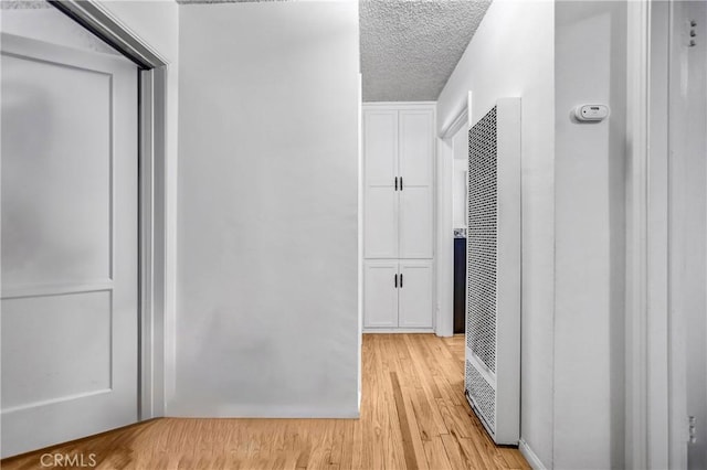 corridor with a textured ceiling and light wood finished floors