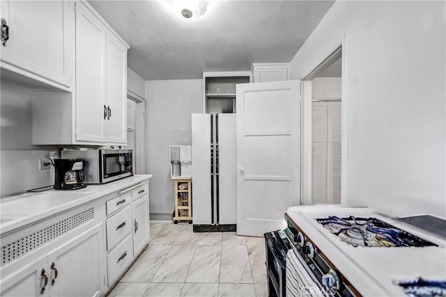 kitchen with marble finish floor, light countertops, stainless steel microwave, freestanding refrigerator, and white cabinetry