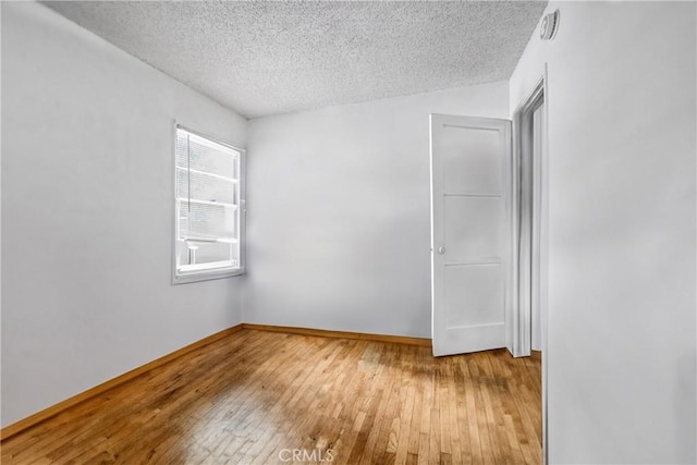 unfurnished room featuring wood-type flooring, baseboards, and a textured ceiling