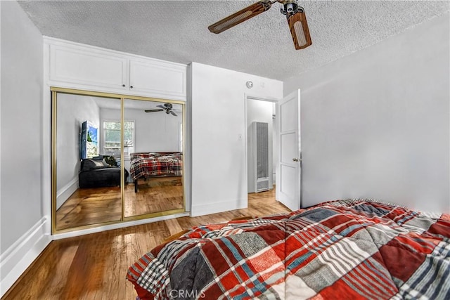 bedroom featuring a closet, a ceiling fan, a textured ceiling, wood finished floors, and baseboards