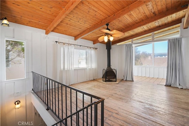 interior space with wood ceiling, hardwood / wood-style floors, beam ceiling, a wood stove, and a decorative wall