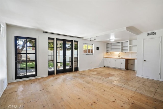 unfurnished living room featuring visible vents, baseboards, light wood-style flooring, french doors, and a sink