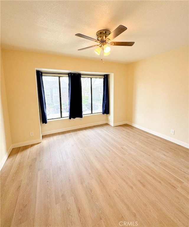 empty room featuring a textured ceiling, light wood-type flooring, a ceiling fan, and baseboards