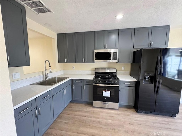 kitchen with light wood finished floors, stainless steel appliances, light countertops, visible vents, and a sink