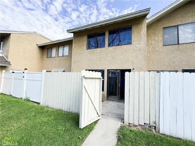 back of house with a gate, fence, a lawn, and stucco siding