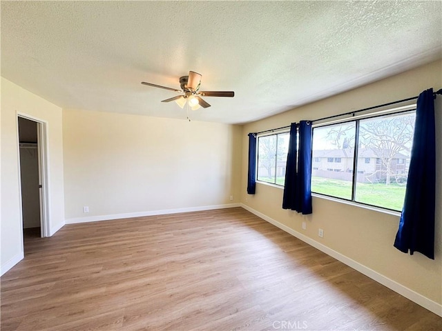 unfurnished room featuring a ceiling fan, light wood-type flooring, a textured ceiling, and baseboards